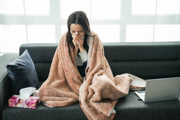istock Young woman with flu sitting on couch looking at laptop 2195339945