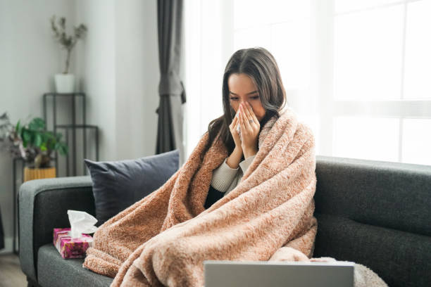 istock Young woman with flu sitting on couch looking at laptop 2195340082