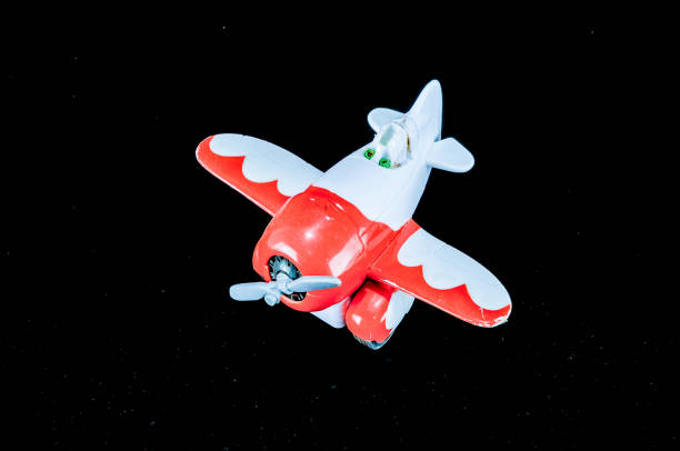 A small red and white toy airplane is flying in the sky. The image has a playful and whimsical mood, as the toy airplane is not a real one but rather a miniature model