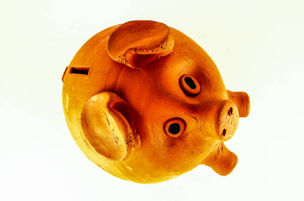 A piggy bank is sitting on a white background. The piggy bank is made of clay and has a brown color