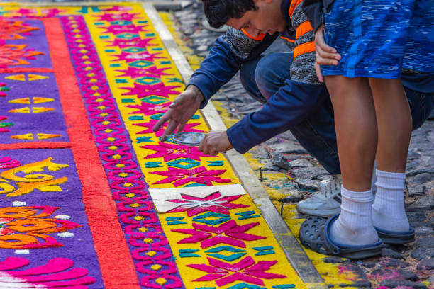 Quito, Pichincha, Ecuador - April 15, 2022: Catholic penitents wearing purple cucuruchos and chains are sitting on the ground taking a rest during the Jesus del Gran Poder procession, a traditional Holy Week celebration in Quito, Ecuador