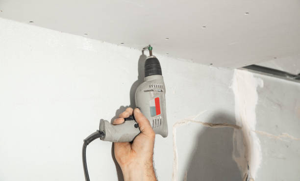 istock Worker with a drill screwdriver twists the screw into the drywall. 2195350961