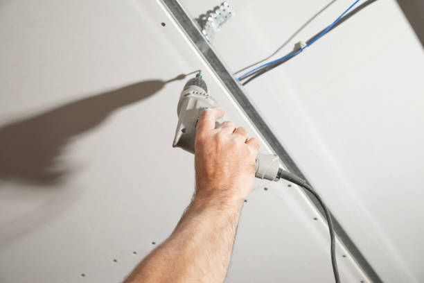 Worker with a drill screwdriver twists the screw into the drywall.