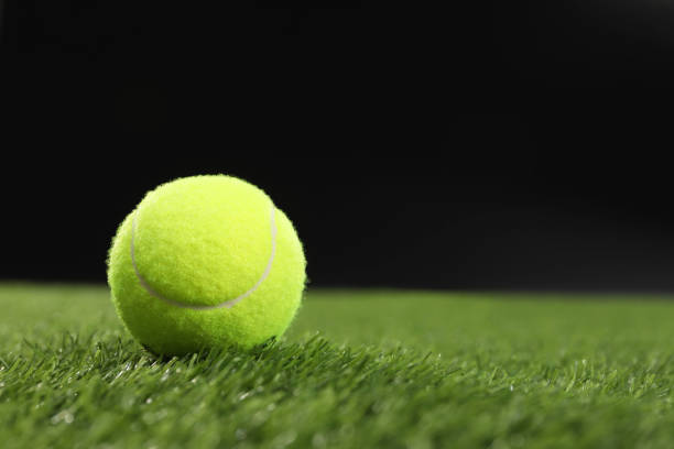 istock Tennis ball on green grass against black background, space for text 2195351834
