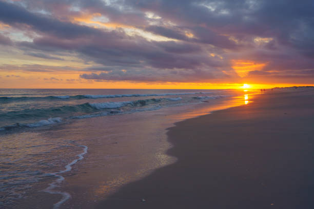 Sunset bursts through the clouds, casting vibrant colors over the ocean and beach