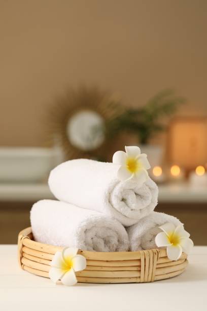 Spa composition. Rolled towels and plumeria flowers on white table indoors. Space for text