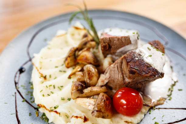 A gourmet dish featuring seared beef steak topped with creamy sauce, accompanied by mashed potatoes and sautéed mushrooms, elegantly plated as a delectable culinary presentation ideal for fine dining settings