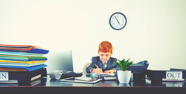 istock Humorous image of happy enthusiastic young boy working on a laptop computer at a desk. He is wearing a suit and working hard. 2195358742