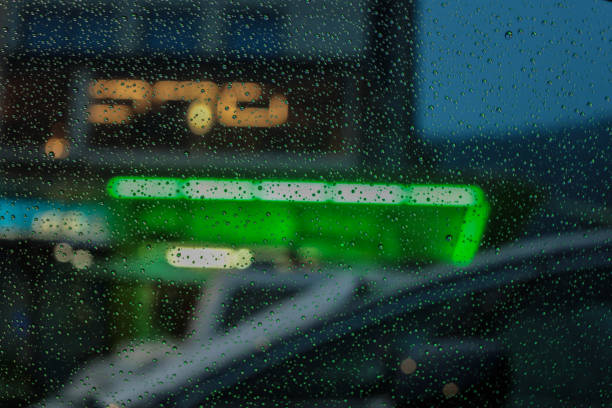 a rainy urban evening through a glass window, with sharp raindrops in the foreground and a blurred background featuring vibrant neon lights in shades of green and blue. The soft, warm glow of additional yellow and orange lights creates a dynamic bokeh effect, adding depth and atmosphere to the scene. The shallow depth of field isolates the raindrops while abstracting the cityscape, evoking feelings of solitude and introspection