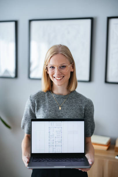 istock Smiling Architect Holding a Laptop Displaying Modern Architectural Floor Plans 2195365603