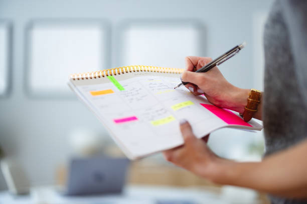 Person Writing Notes in Planner with Colorful Sticky Notes in Bright Office Environment