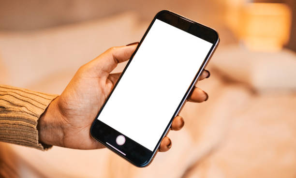 Close-up of a woman's hand holding a mobile phone with blank screen in a bedroom. The scene symbolizes technology, communication, and modern digital lifestyles in a relaxed setting
