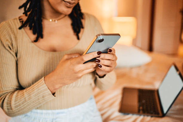 istock Woman Using Mobile Phone with Laptop on Bed in Background 2195370550