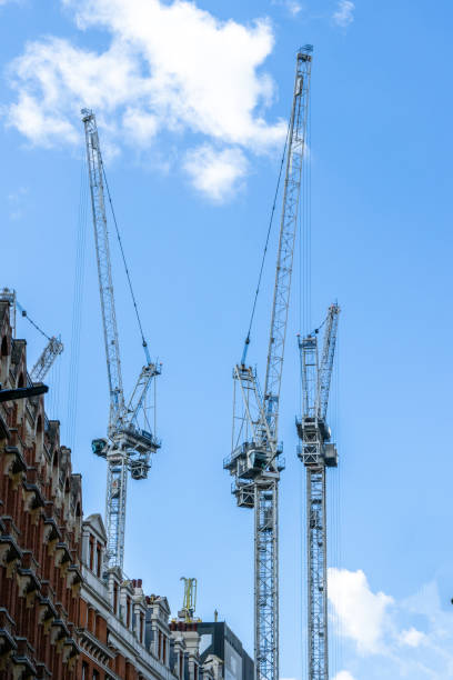 An upward view of contemporary glass and steel buildings in London, reflecting the surrounding cityscape. A construction crane in the background highlights ongoing urban development and modern architectural design in the bustling metropolis.
