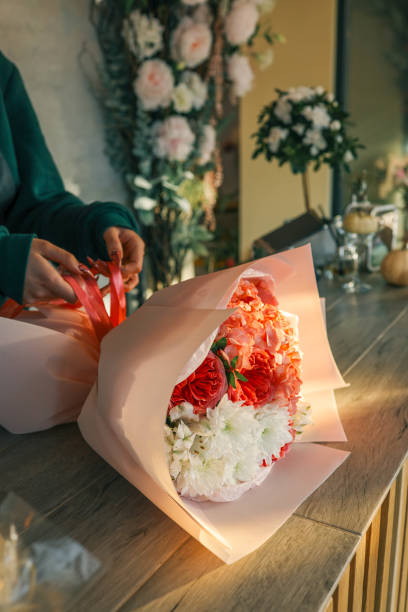 istock Close-up of a luxurious bouquet featuring vibrant red roses, delicate hydrangeas, and white alstroemerias, elegantly arranged and wrapped in soft pastel paper on a wooden counter 2195388352