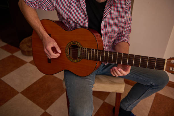 Man playing an acoustic guitar while sitting indoors on a chair