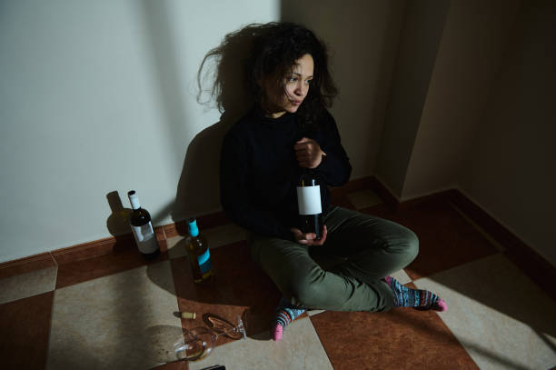 istock Woman reflecting with wine bottles during loneliness in low-lit setting 2195391185