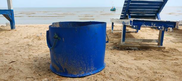 Blue bucket on sandy beach with ocean and beach chair.