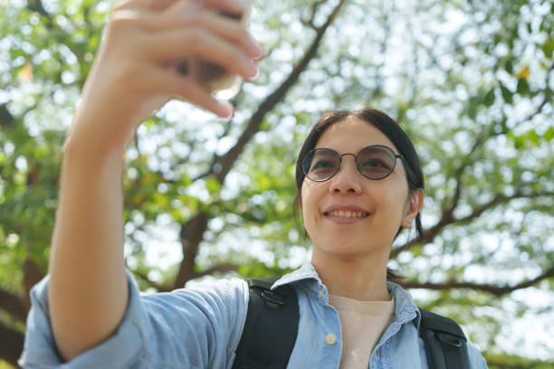 istock An Asian woman in a denim jacket taking a selfie outdoors in a forest, surrounded by greenery. 2195406701