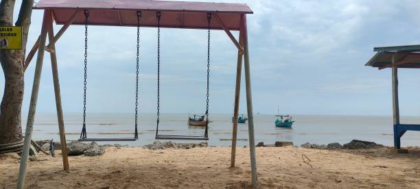 istock Empty swing set on a sandy beach overlooking calm water with distant boats. 2195407666