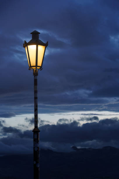 Glowing street lamp against dark clouds at dusk
