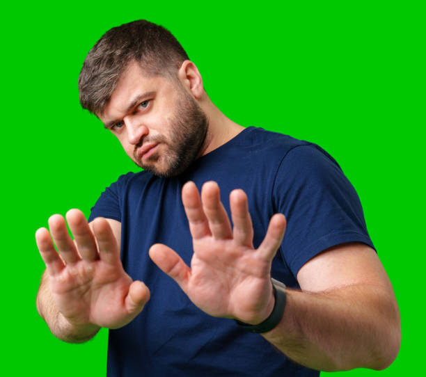istock A man with a serious expression holds up both hands in a stopping gesture against a bright green background 2195413170