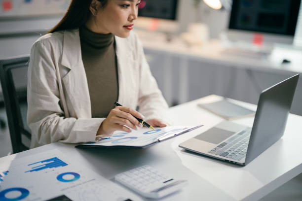 istock Professional businesswoman analyzing financial charts, typing on laptop while working intently at sleek office workspace 2195417247