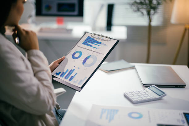 istock Professional female executive reviewing financial data on clipboard, working at sleek workspace with laptop and calculator in contemporary office setting 2195417266