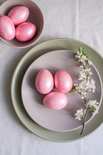 istock Easter table setting with minimalist floral decor. Pastel pink Easter eggs in a gray plate on linen tablecloth 2195426387