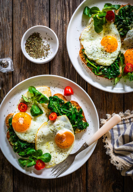 istock Crispy toast with stewed spinach and fried eggs with runny yolks on wooden table 2195428330