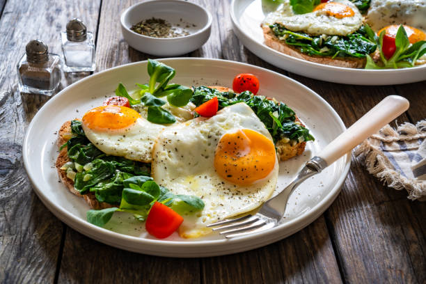 istock Crispy toast with stewed spinach and fried eggs with runny yolks on wooden table 2195428795