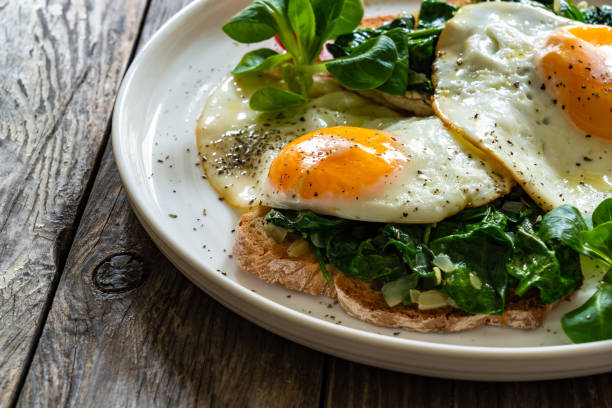 istock Crispy toast with stewed spinach and fried eggs with runny yolks on wooden table 2195428898