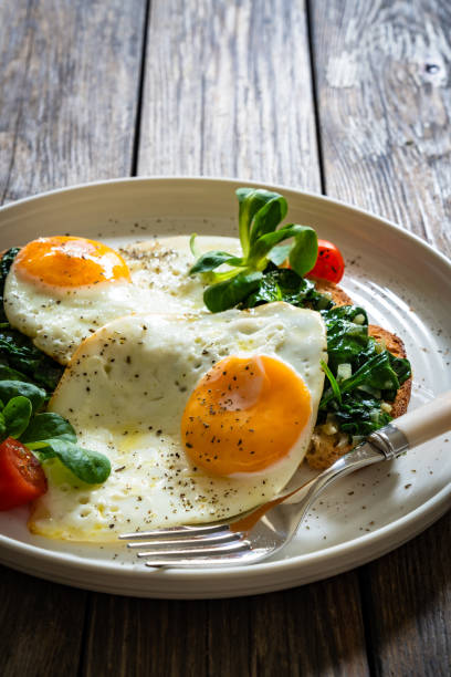 istock Crispy toast with stewed spinach and fried eggs with runny yolks on wooden table 2195428923