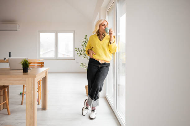 istock Woman Looking Outside While Holding a Cup of Coffee 2195431797