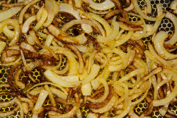 Close-up view of golden caramelized onions being fried in oil on a textured frying pan. Capturing the rich texture and appetizing visual of sizzling, browned onions, ideal for cooking and food concepts.