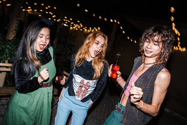 istock Three friends enjoying drinks and laughing together at an outdoor night party. Warm string lights and festive vibes create an energetic and joyful scene. 2195434565
