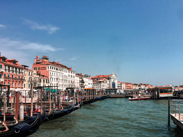 This photo captures a quintessential Venetian scene. A bustling canal is lined with colorful buildings and filled with gondolas, creating a lively and picturesque atmosphere. The clear blue sky adds to the vibrant feel of the image. It evokes a sense of exploration and invites the viewer to imagine a leisurely boat ride through this enchanting city.