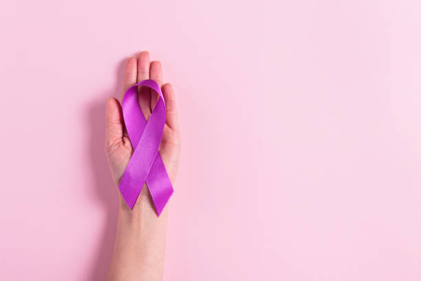 istock Purple ribbon in womans hand on pink background 2195439745