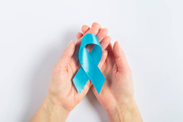istock Blue ribbon in hand for cancer awareness on white background 2195439748