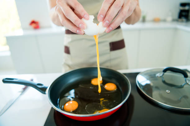 istock Woman cracking eggs into pan while preparing meal in bright kitchen with apron, highlighting home cooking and nutrition 2195444256