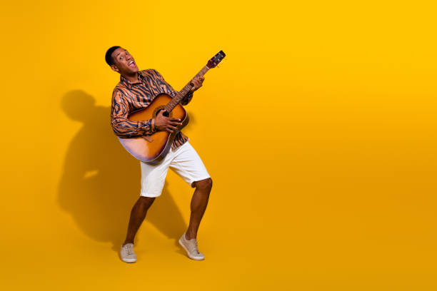 istock Cheerful young man playing guitar enthusiastically against bright yellow background, enjoying music and being vibrant and fashionable 2195447655