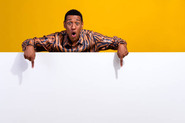 istock Cheerful young man pointing below with expressive gesture on a vibrant yellow background 2195447802