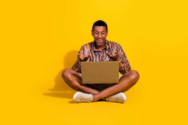 istock Happy young man using a laptop on a vibrant yellow background, showing a surprised expression and wearing a trendy casual outfit 2195447849