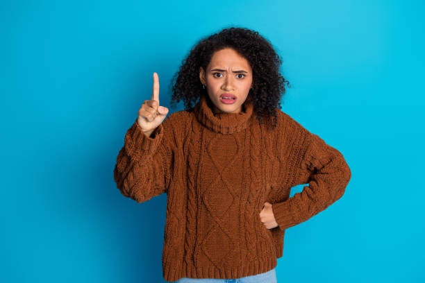 istock Young woman expressing confusion with a pointing gesture against a blue background 2195449247