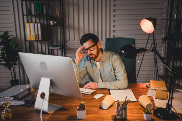 istock Young man working at his desk in a modern office during nighttime under warm light 2195452654