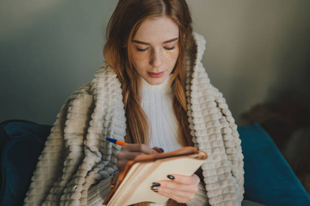 istock A woman is writing in her journal while feeling cozy and comfortable in her home environment 2195456174