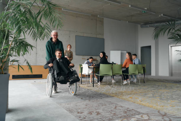 istock A diverse and multicultural business team collaborates in the office while their colleagues, including a director in a wheelchair and his friend, share a lighthearted moment, fostering an atmosphere of support and camaraderie 2195456603