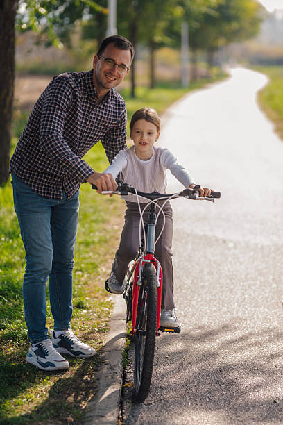 istock Father teaching daughter how to ride bicycle in park 2195458447