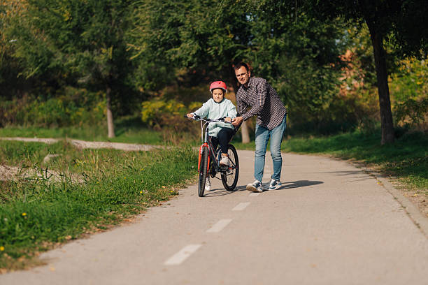 istock Father teaching daughter riding bicycle in park during summer day 2195458504