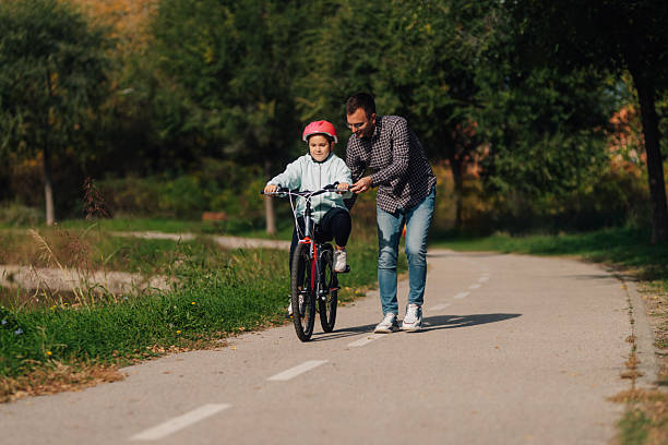 Father teaching his daughter to ride a bicycle in a park, enjoying quality time together on a beautiful sunny day
